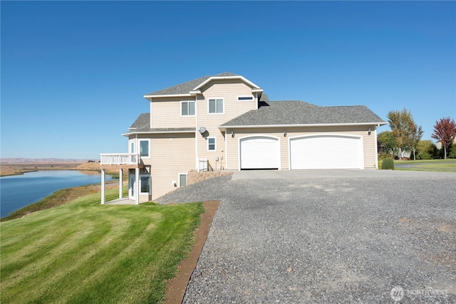 view of front facade featuring an attached garage, a water view, driveway, roof with shingles, and a front yard