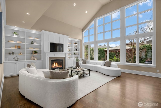 living room featuring high vaulted ceiling, dark wood-style flooring, a glass covered fireplace, and baseboards