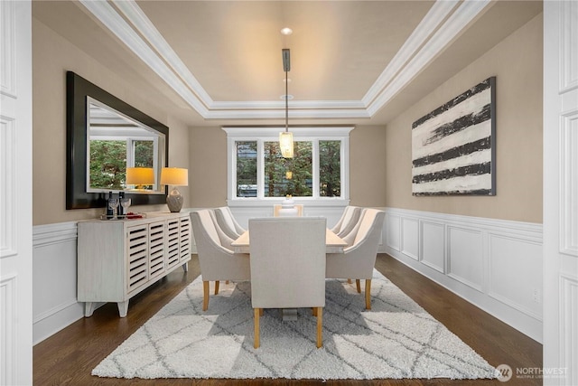dining area featuring wainscoting, dark wood-style flooring, crown molding, and a raised ceiling