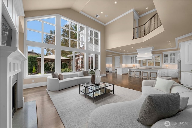 living area featuring a fireplace with flush hearth, wood finished floors, visible vents, and high vaulted ceiling