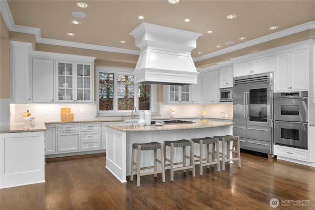 kitchen with built in appliances, white cabinets, a center island, and glass insert cabinets
