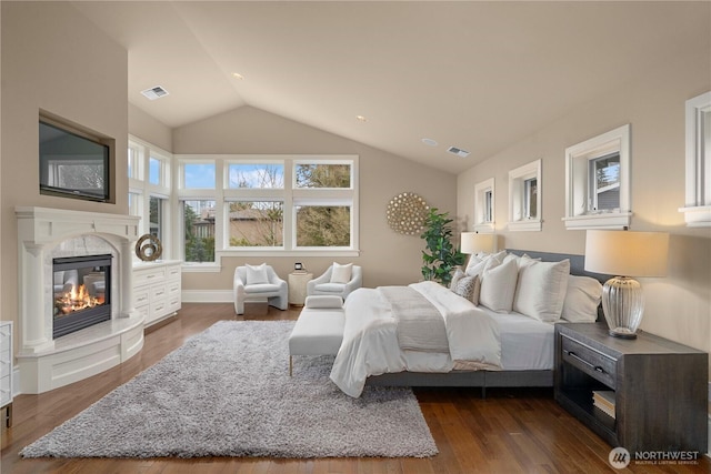 bedroom featuring a high end fireplace, vaulted ceiling, dark wood-style flooring, and visible vents