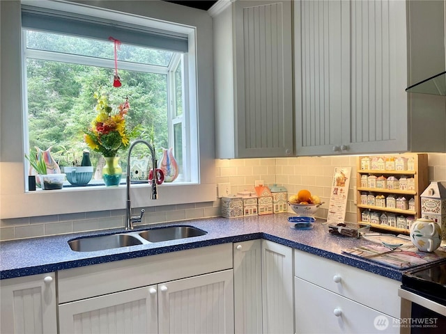 kitchen with tasteful backsplash, dark countertops, a sink, and white cabinets