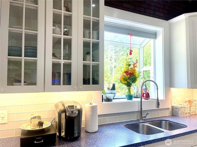 kitchen with backsplash, a sink, glass insert cabinets, and white cabinetry