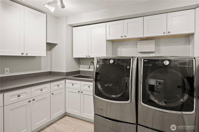 washroom featuring washing machine and clothes dryer, cabinet space, light wood-style floors, a sink, and track lighting