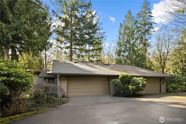 view of front of home with a garage, driveway, and roof with shingles