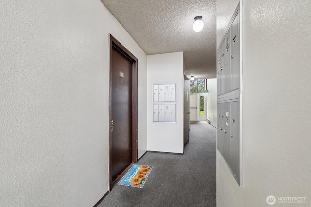 corridor with a textured wall, mail area, a textured ceiling, and carpet flooring