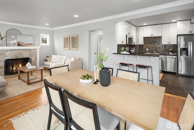 dining room with dark wood finished floors, a tiled fireplace, recessed lighting, and ornamental molding