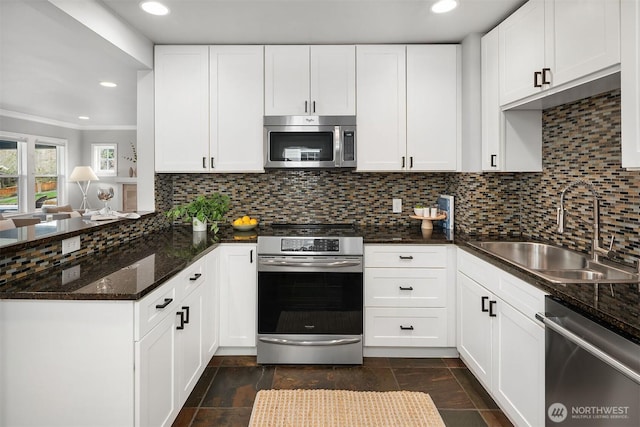 kitchen with decorative backsplash, a peninsula, white cabinets, stainless steel appliances, and a sink