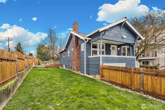 rear view of house with a chimney, a yard, and fence