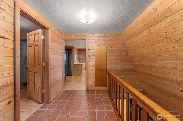 corridor with wood walls, a textured ceiling, and dark tile patterned floors