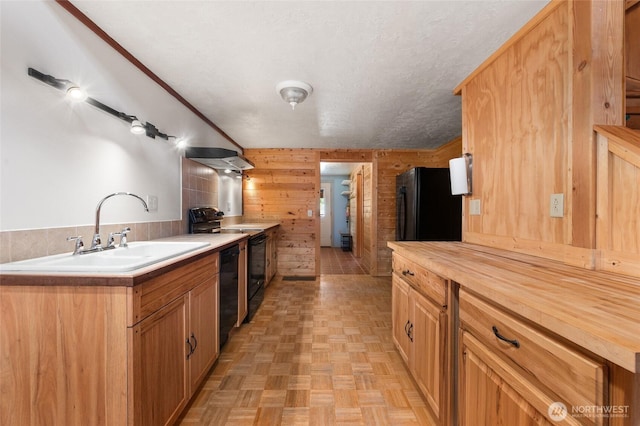 kitchen featuring wooden counters, a sink, a textured ceiling, wood walls, and black appliances