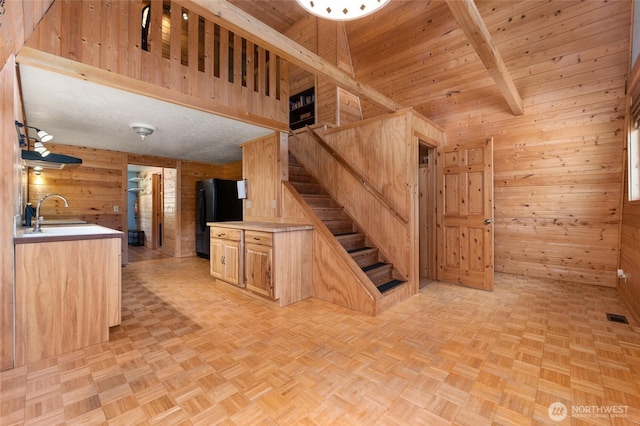 kitchen featuring wooden walls, a sink, visible vents, freestanding refrigerator, and beamed ceiling