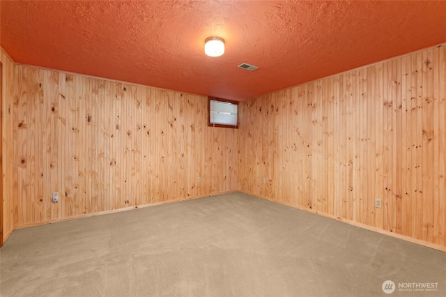 carpeted empty room featuring a textured ceiling, visible vents, and wooden walls