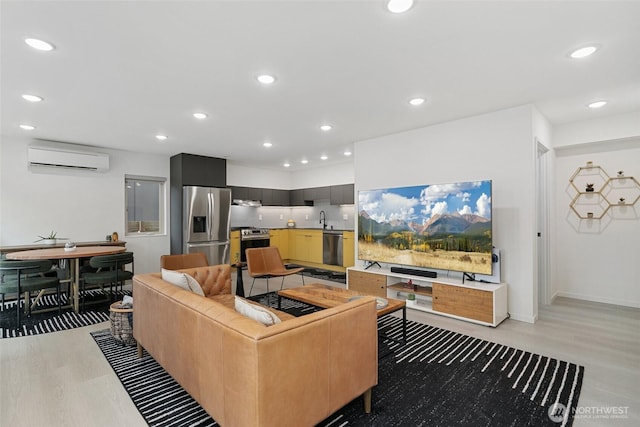 living area featuring a wall unit AC, light wood finished floors, baseboards, and recessed lighting