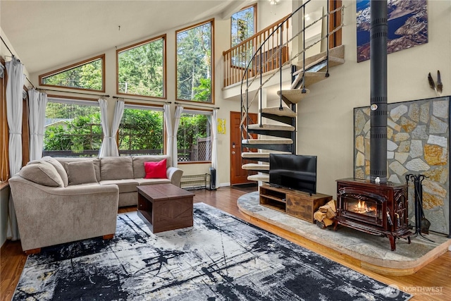 living room with high vaulted ceiling, a baseboard radiator, wood finished floors, stairway, and a wood stove