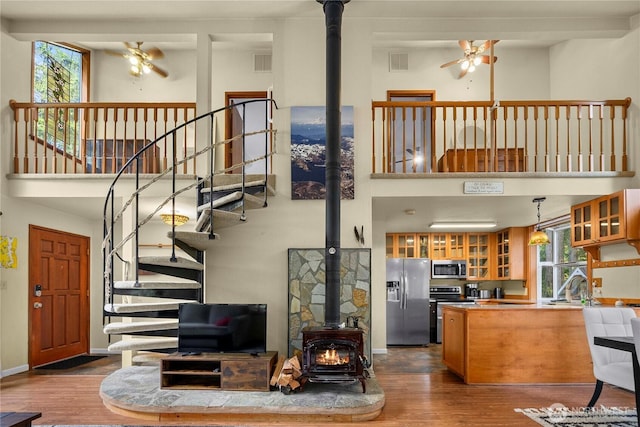 living room with dark wood-style flooring, visible vents, a towering ceiling, a ceiling fan, and a wood stove