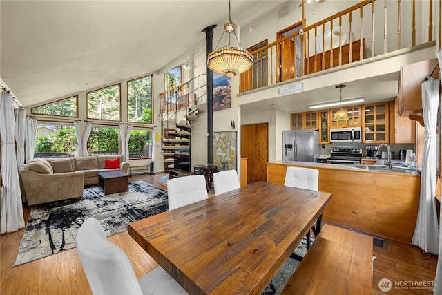 dining room featuring high vaulted ceiling, light wood-style flooring, stairs, and visible vents