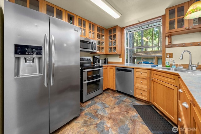 kitchen with glass insert cabinets, stone finish floor, appliances with stainless steel finishes, and a sink