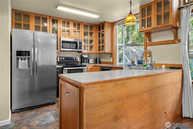 kitchen with appliances with stainless steel finishes, glass insert cabinets, a peninsula, stone finish flooring, and a sink