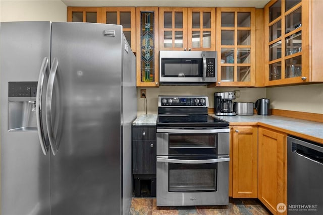 kitchen with stainless steel appliances, stone finish flooring, light countertops, and glass insert cabinets