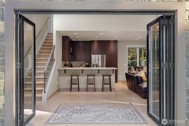 kitchen with stainless steel fridge with ice dispenser, a breakfast bar area, a peninsula, light countertops, and dark brown cabinets