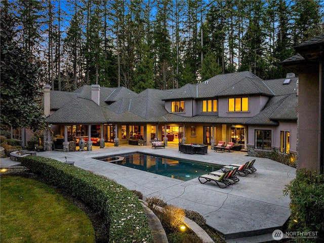 rear view of property featuring a patio, an outdoor pool, an outdoor living space with a fire pit, and stucco siding