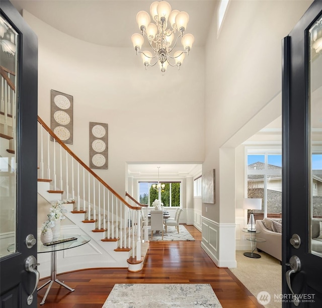 entrance foyer featuring stairway, an inviting chandelier, wood finished floors, and a towering ceiling