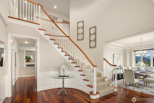 stairs with an inviting chandelier, ornamental molding, a towering ceiling, and wood-type flooring