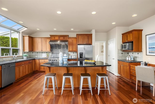 kitchen with dark wood-type flooring, under cabinet range hood, a center island, stainless steel appliances, and a breakfast bar area