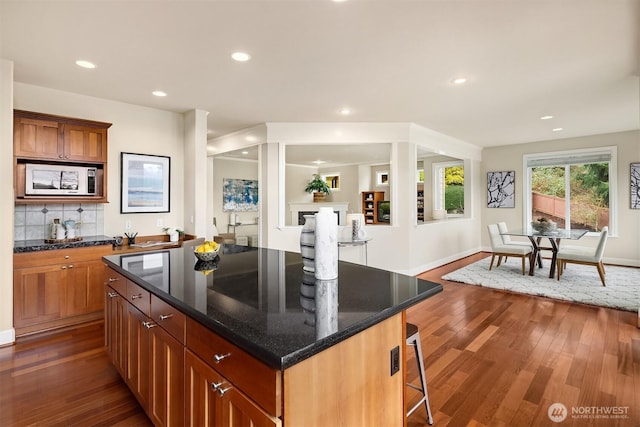 kitchen with dark wood-type flooring, stainless steel microwave, a center island, a breakfast bar area, and decorative backsplash