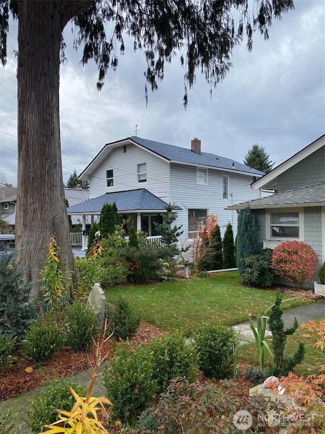 rear view of property featuring a shingled roof, a lawn, and a chimney