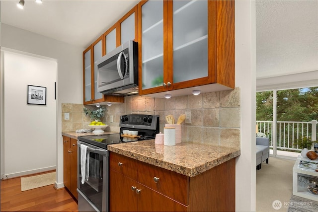 kitchen featuring appliances with stainless steel finishes, glass insert cabinets, light wood-style flooring, and tasteful backsplash