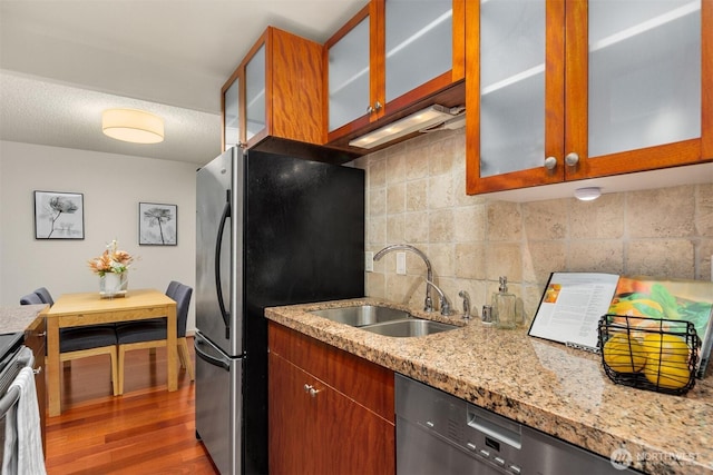 kitchen featuring tasteful backsplash, glass insert cabinets, wood finished floors, stainless steel appliances, and a sink