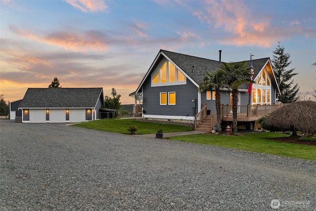 view of front of property with a deck, roof with shingles, a lawn, and gravel driveway