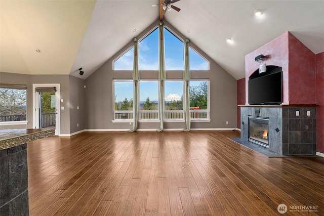 unfurnished living room featuring high vaulted ceiling, baseboards, a tiled fireplace, and hardwood / wood-style flooring