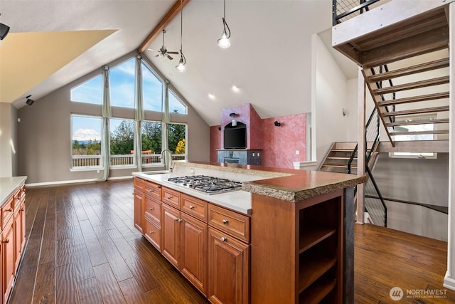 kitchen with ceiling fan, dark wood-style flooring, a sink, a center island with sink, and stainless steel gas stovetop