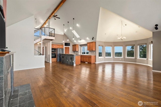 unfurnished living room featuring baseboards, dark wood finished floors, a fireplace, high vaulted ceiling, and ceiling fan with notable chandelier