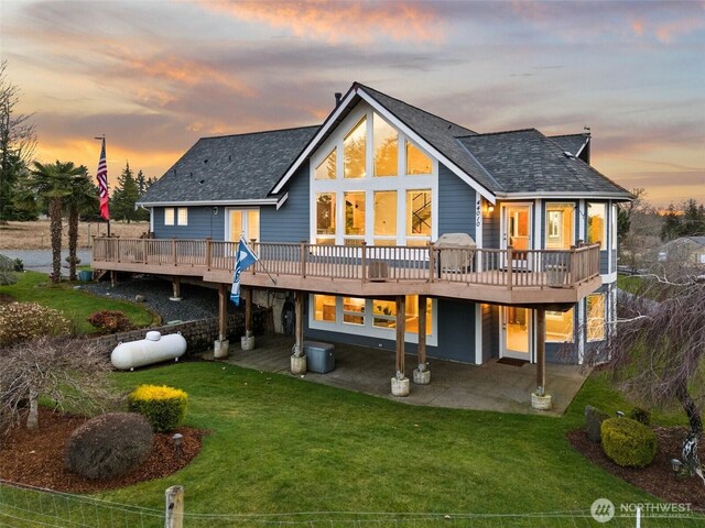 back of house at dusk featuring a patio area, a lawn, and a deck