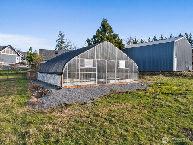 exterior space featuring a greenhouse, a lawn, and an outdoor structure