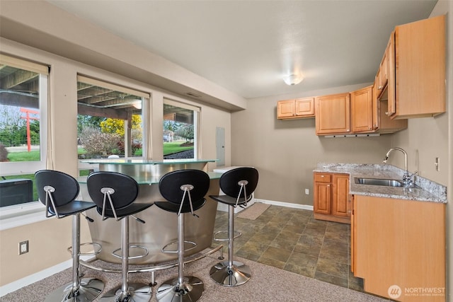 kitchen with a sink, baseboards, light stone countertops, light brown cabinetry, and stone finish floor