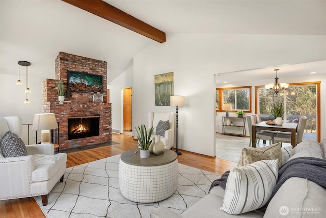 living room with vaulted ceiling with beams, a brick fireplace, wood finished floors, and an inviting chandelier