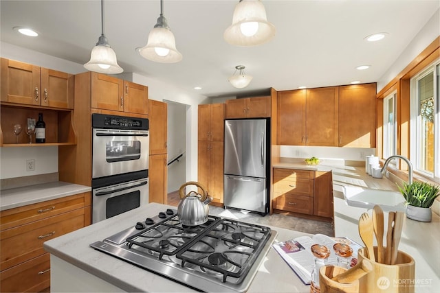 kitchen with light countertops, hanging light fixtures, appliances with stainless steel finishes, brown cabinetry, and a sink