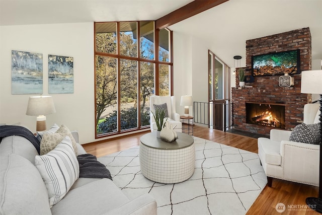 living room featuring vaulted ceiling with beams, a brick fireplace, and wood finished floors