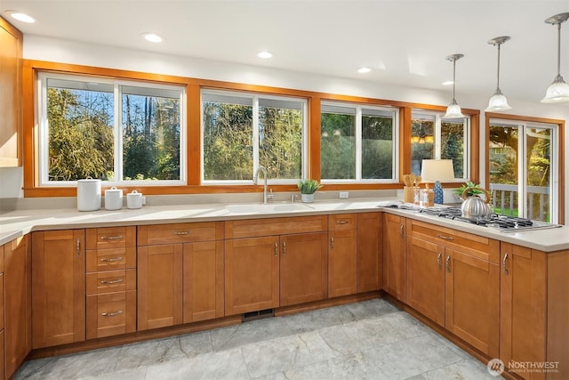 kitchen featuring recessed lighting, a sink, hanging light fixtures, light countertops, and brown cabinetry