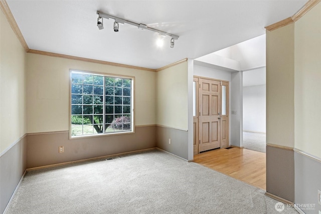 carpeted spare room with baseboards, ornamental molding, visible vents, and track lighting