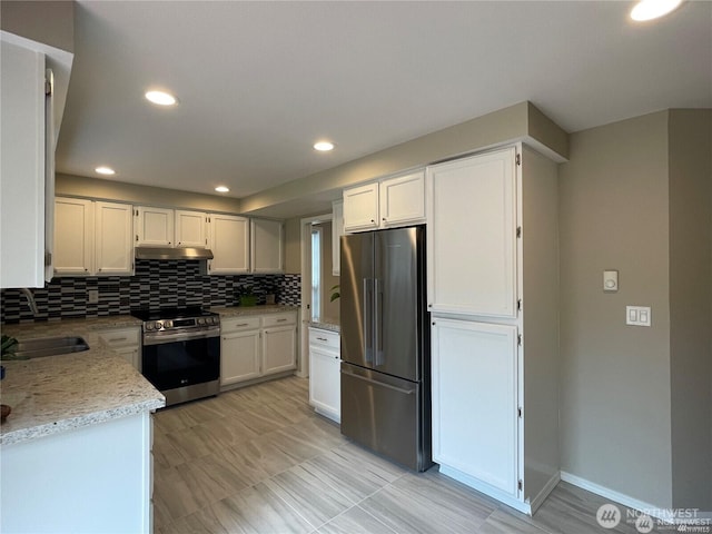 kitchen with stainless steel appliances, a sink, white cabinetry, decorative backsplash, and light stone countertops