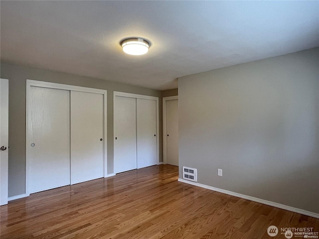 unfurnished bedroom featuring baseboards, visible vents, two closets, and wood finished floors