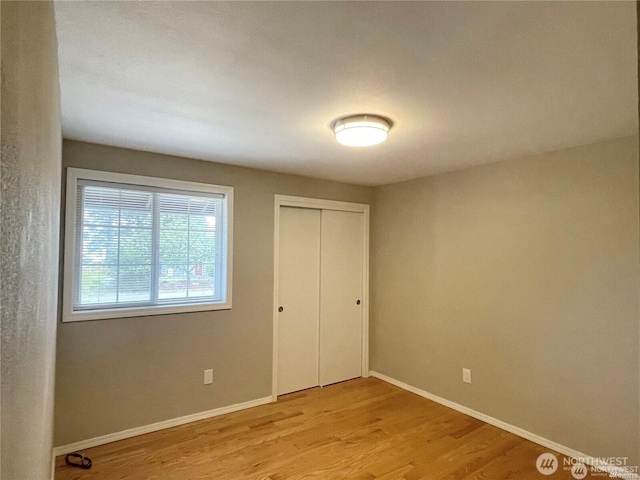 unfurnished bedroom with light wood-style flooring, baseboards, and a closet