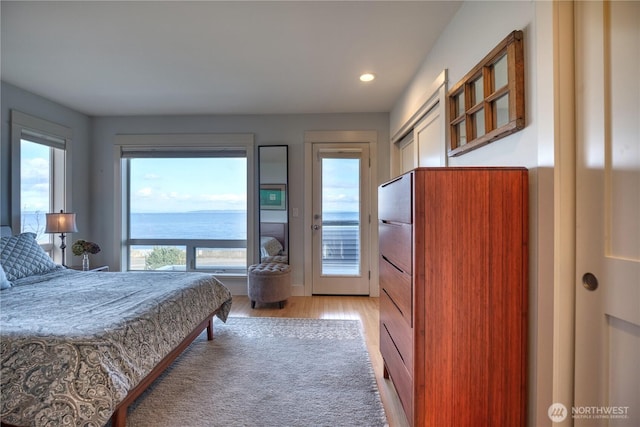 bedroom with light wood finished floors, a water view, recessed lighting, and access to exterior